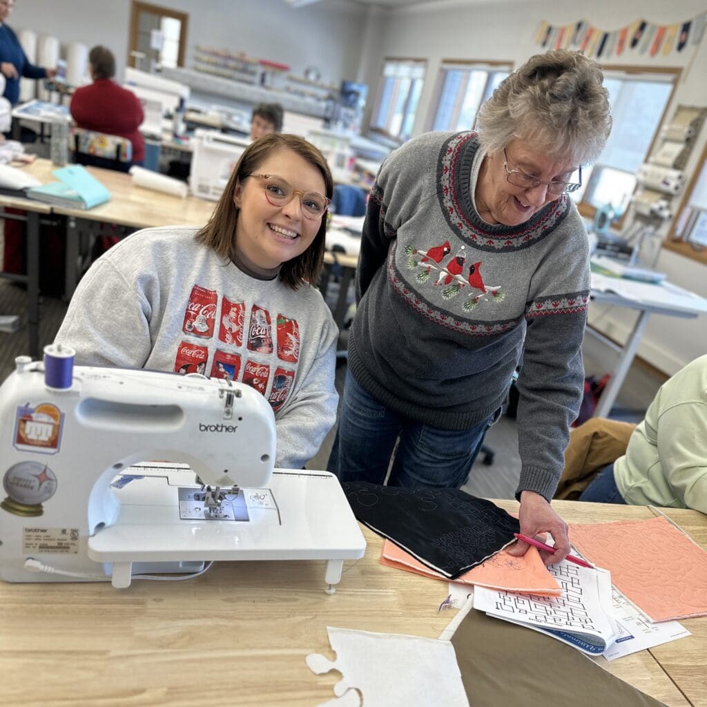 Two women sewing and smiling in workshop.
