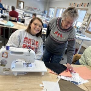 Two women sewing and smiling in workshop.