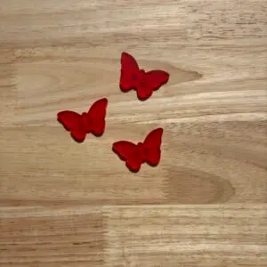 Three red butterfly buttons on wooden surface