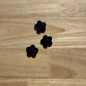 Three purple flower-shaped beads on wood
