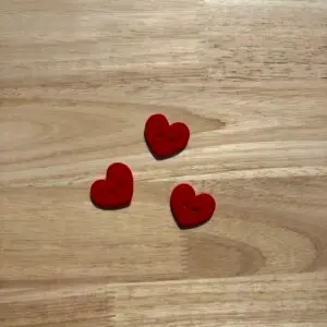 Three red heart-shaped buttons on wooden table