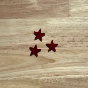 Three red star-shaped sequins on wooden table