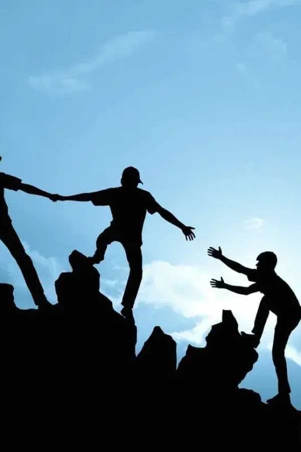 Silhouetted hikers helping each other up cliff